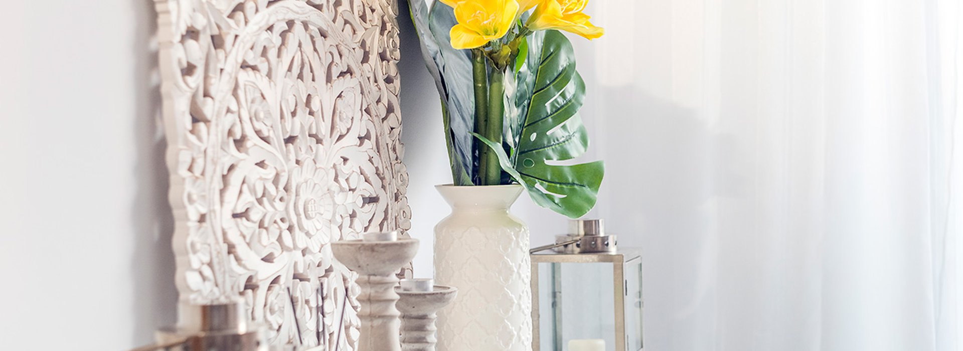 Yellow flowers in ceramic vase with wooden candlesticks and lantern decorating a shelf